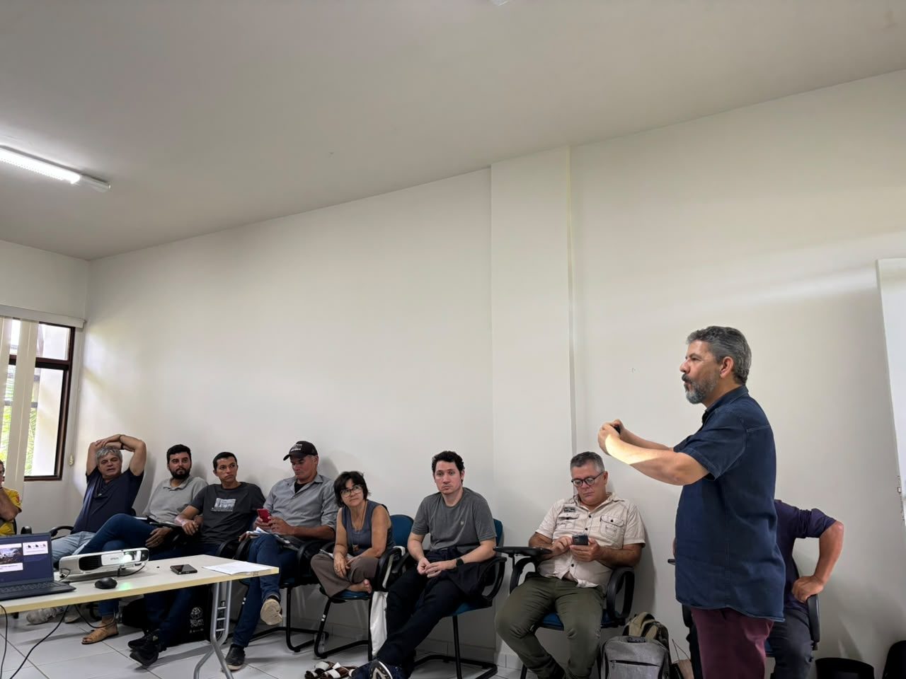 Pessoa em pé conduzindo uma atividade com o grupo sentado à mesa
